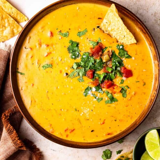 bowl of crockpot queso garnished with tomatoes and cilantro with tortilla chips