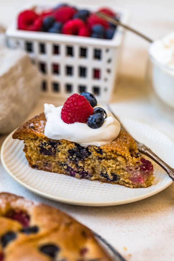 A slice of Blueberry Raspberry Coffee Cake topped with cream