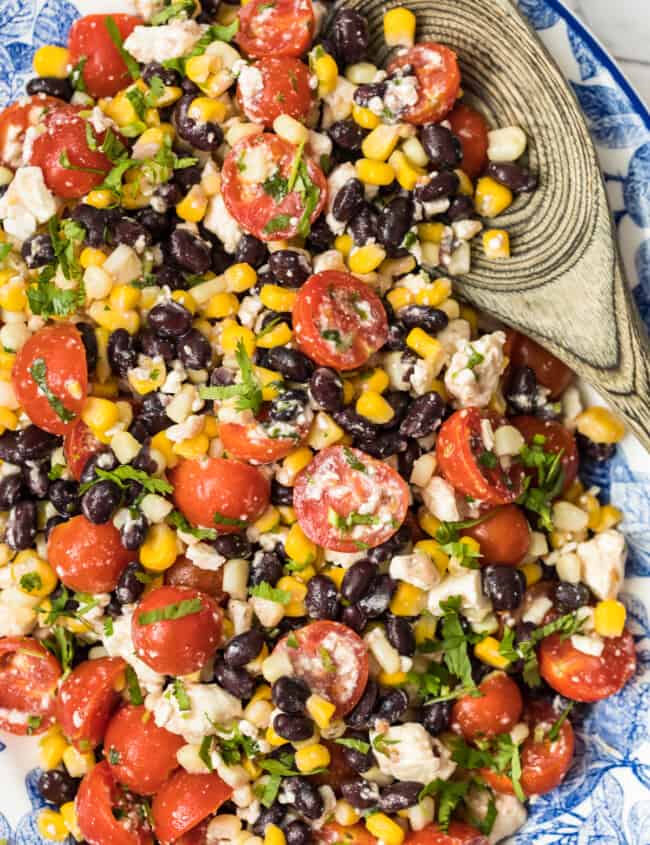 tomato corn salad on platter with wooden spoon