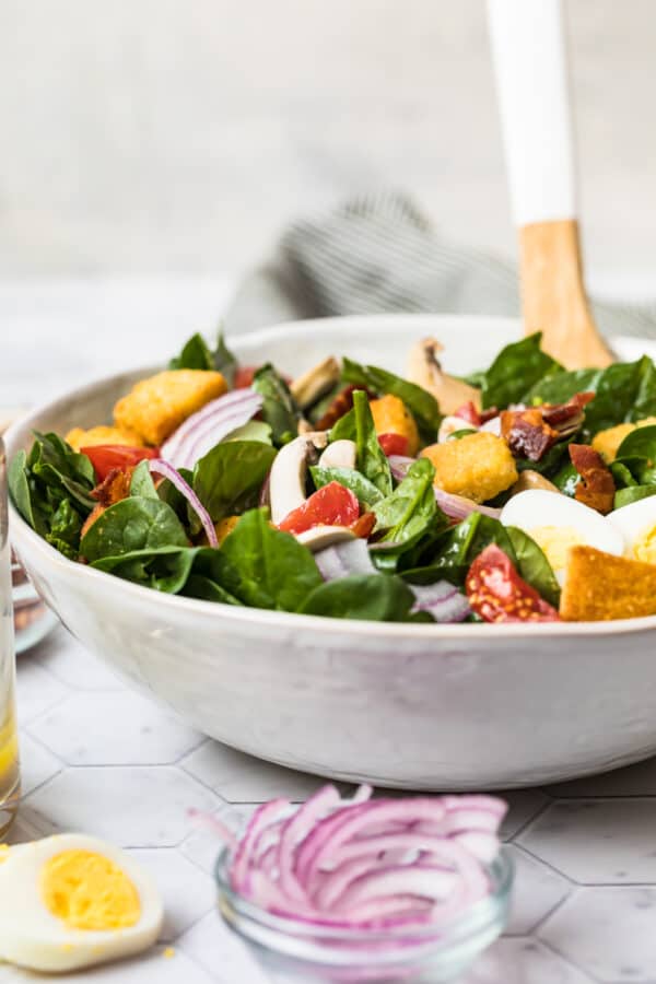 side shot of spinach salad with bacon and hard boiled egg in white bowl