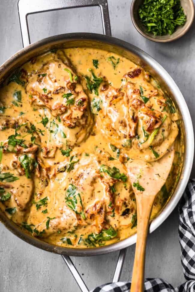 side shot of tuscan chicken in cream sauce with wooden spoon