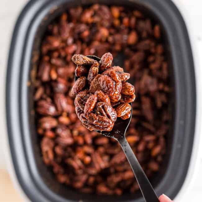 lifting up spoonful of crockpot candied nuts