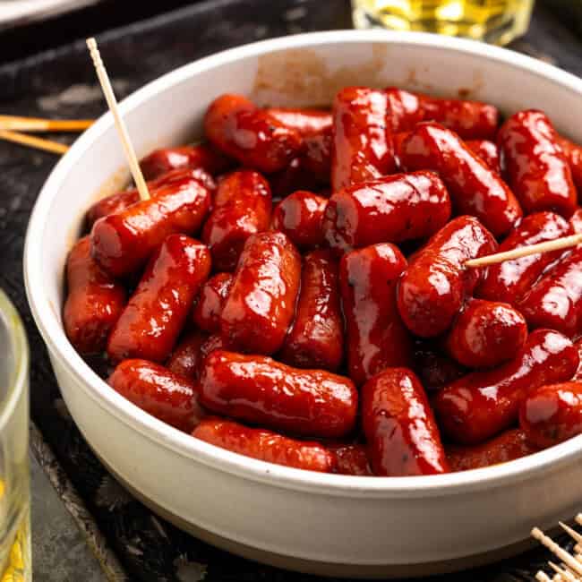 little smokies sausages in a white bowl with toothpicks.