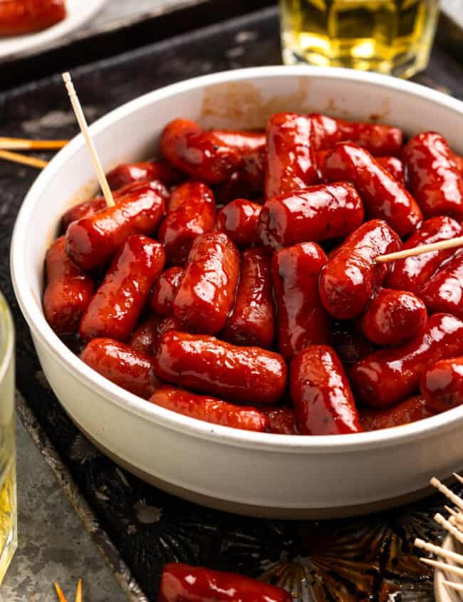 little smokies sausages in a white bowl with toothpicks.