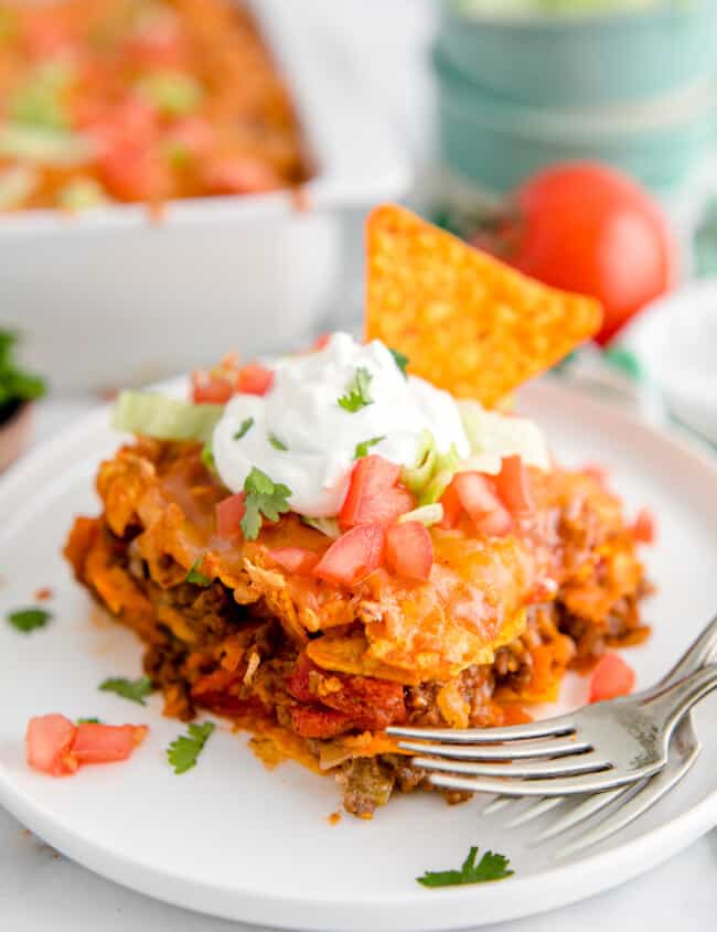 slice of dorito casserole garnished with sour cream and chopped tomatoes