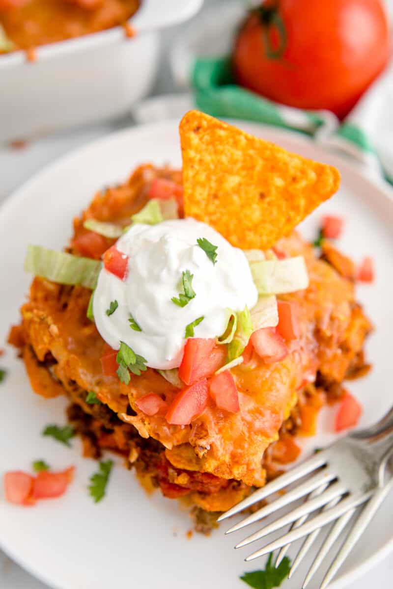 slice of dorito casserole garnished with sour cream and chopped tomatoes