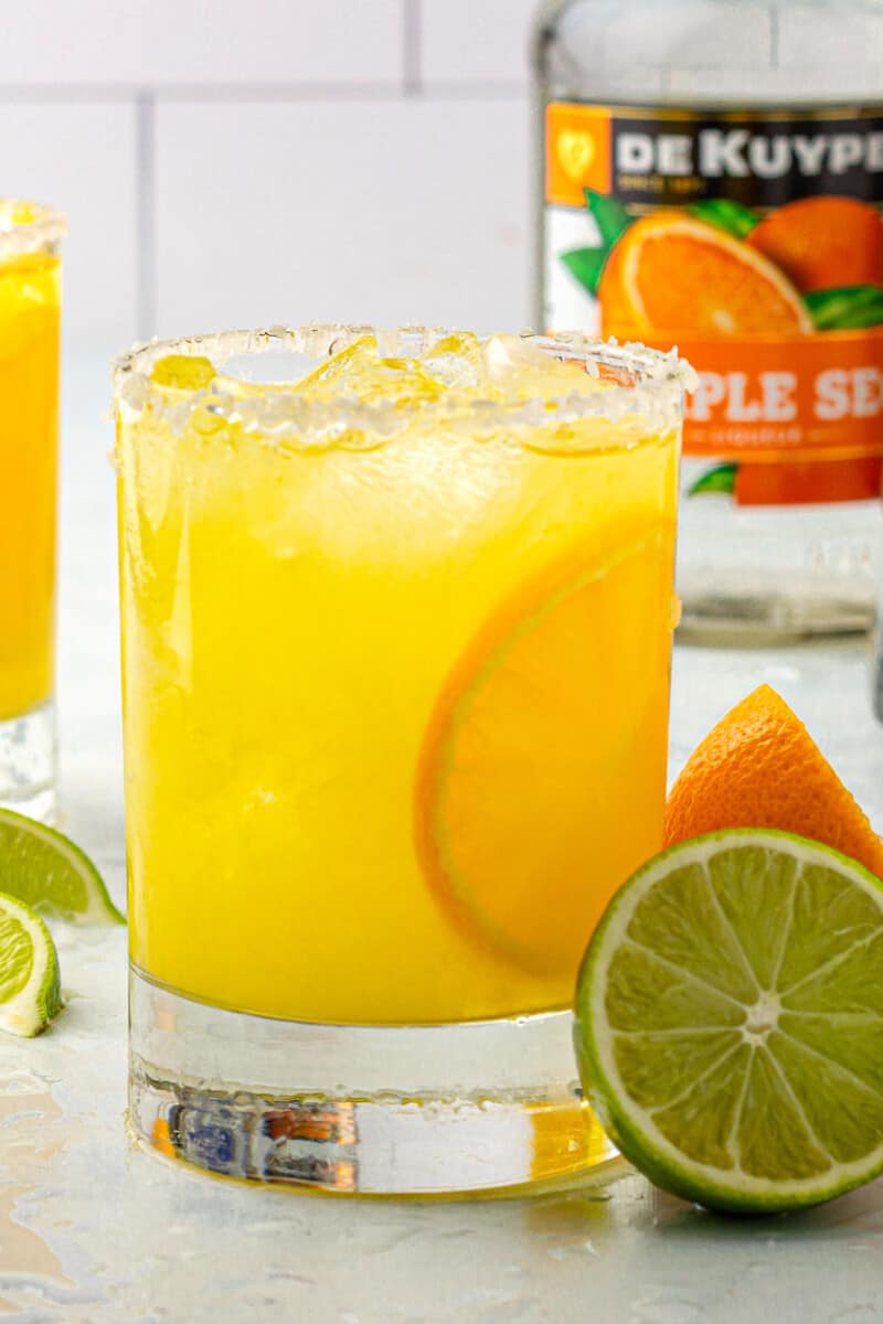 orange margarita with orange and lime slices next to triplesec