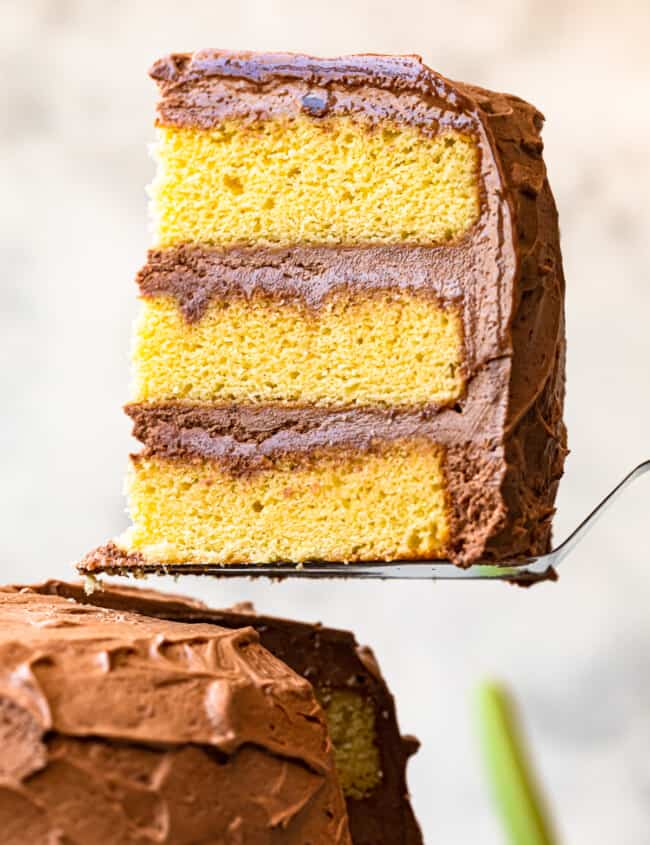 lifting up slice of yellow layer cake with milk chocolate frosting