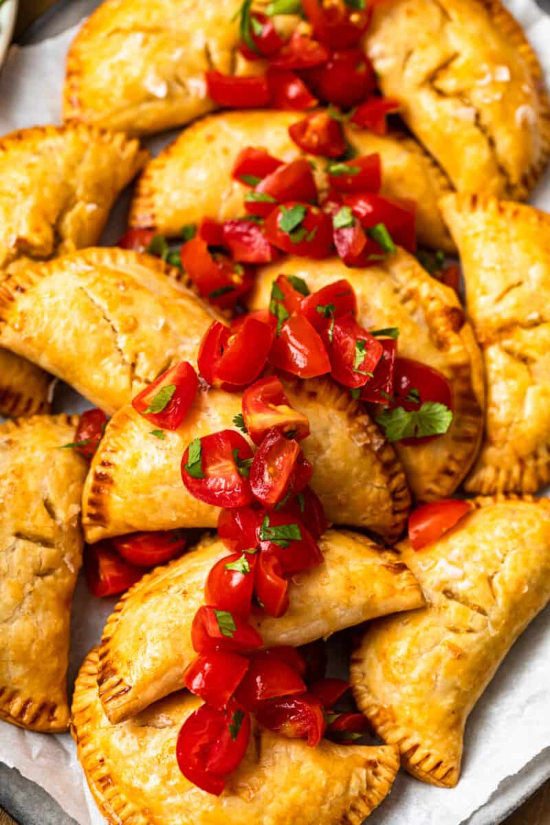 baked chicken empanadas on platter garnished with tomatoes