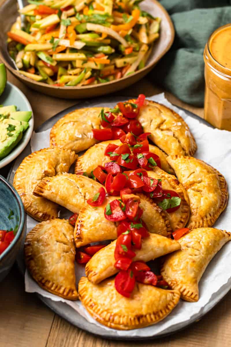 baked chicken empanadas on platter garnished with tomatoes next to jicama slaw