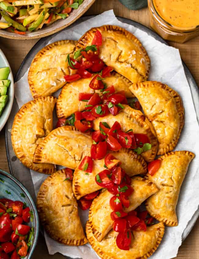 overhead baked chicken empanadas on platter garnished with tomatoes