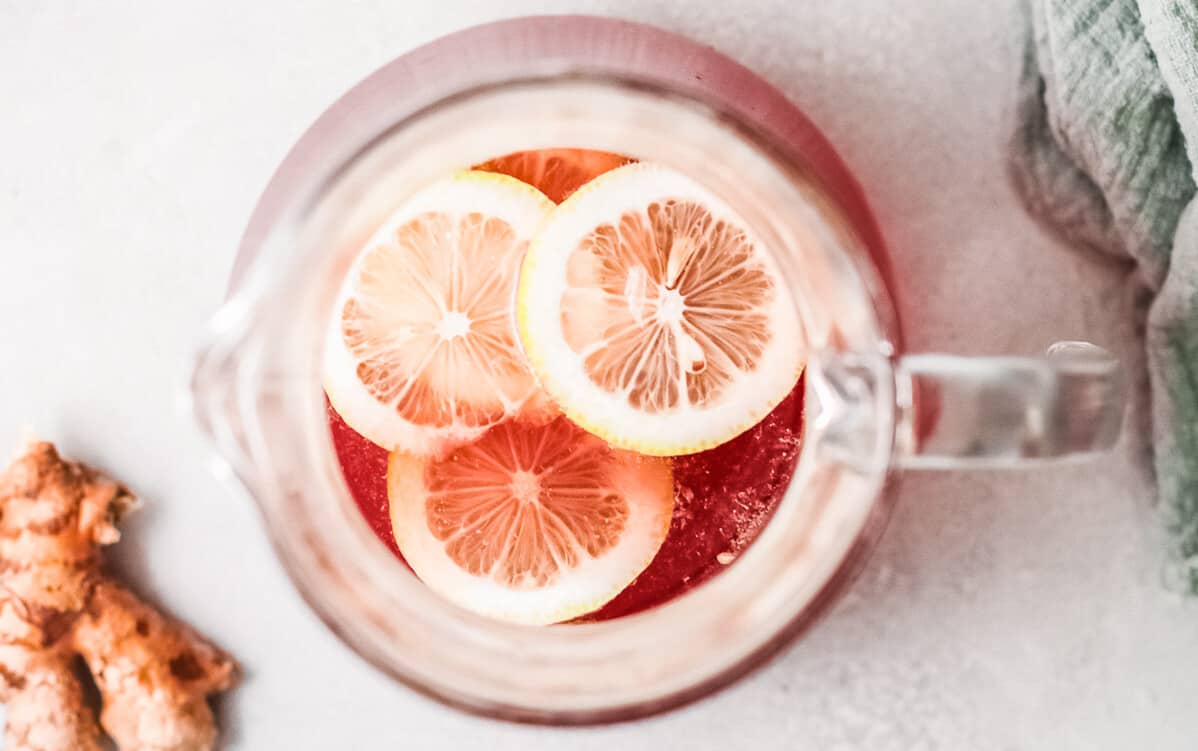 A pitcher of ginger lemonade with slices of lemon and ginger, served alongside a refreshing cranberry margarita.