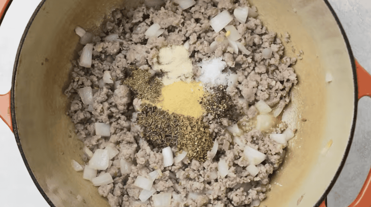 spices and mustard over cooked crumbled sausage and onion in a Dutch oven.