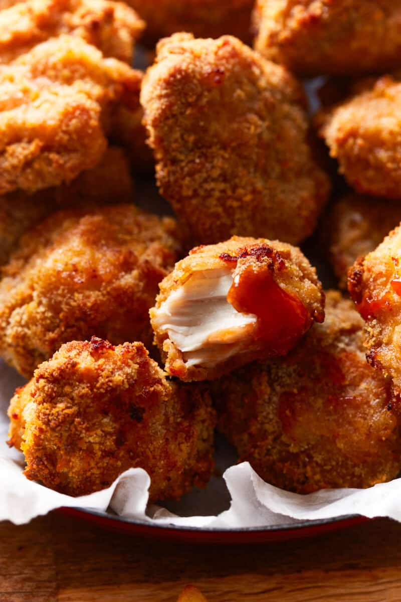 a bitten air fryer chicken nugget on top of a pile of nuggets in a parchment lined basket.