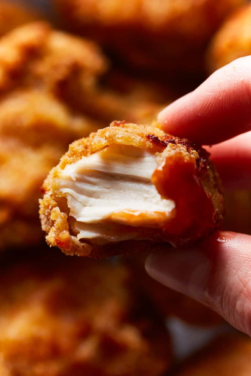 close up of a hand holding a bitten air fryer chicken nugget.