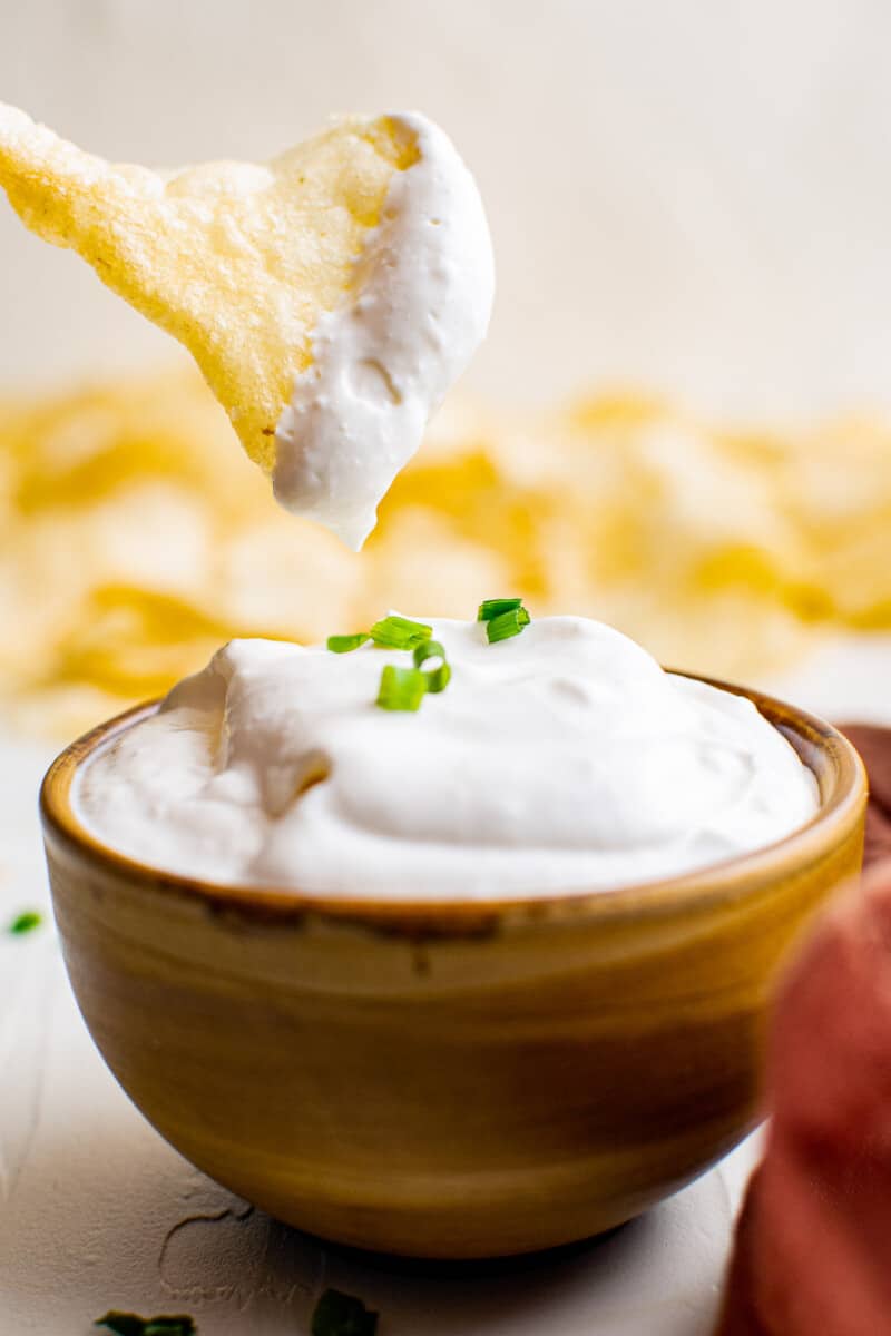 A potato chip being dipped into sour cream and onion dip.