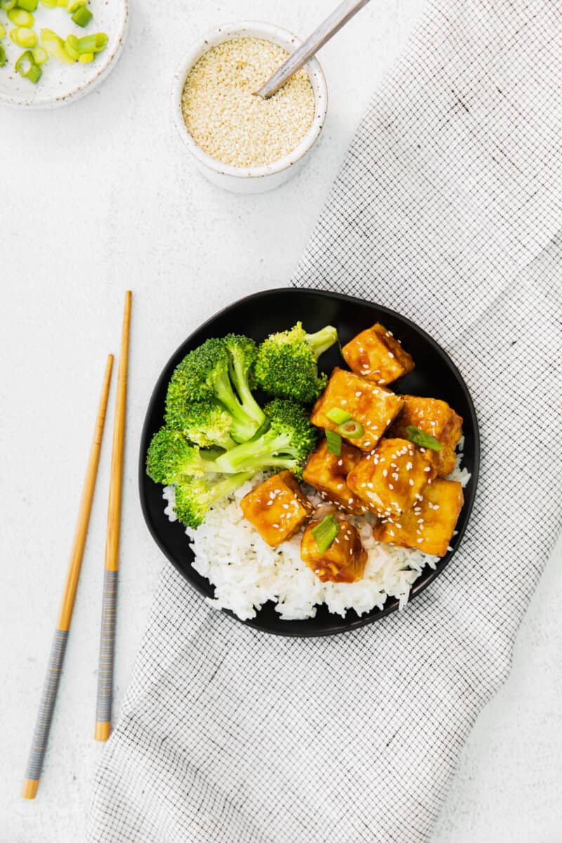 overhead view of air fryer teriyaki tofu on a black plate with chopsticks.