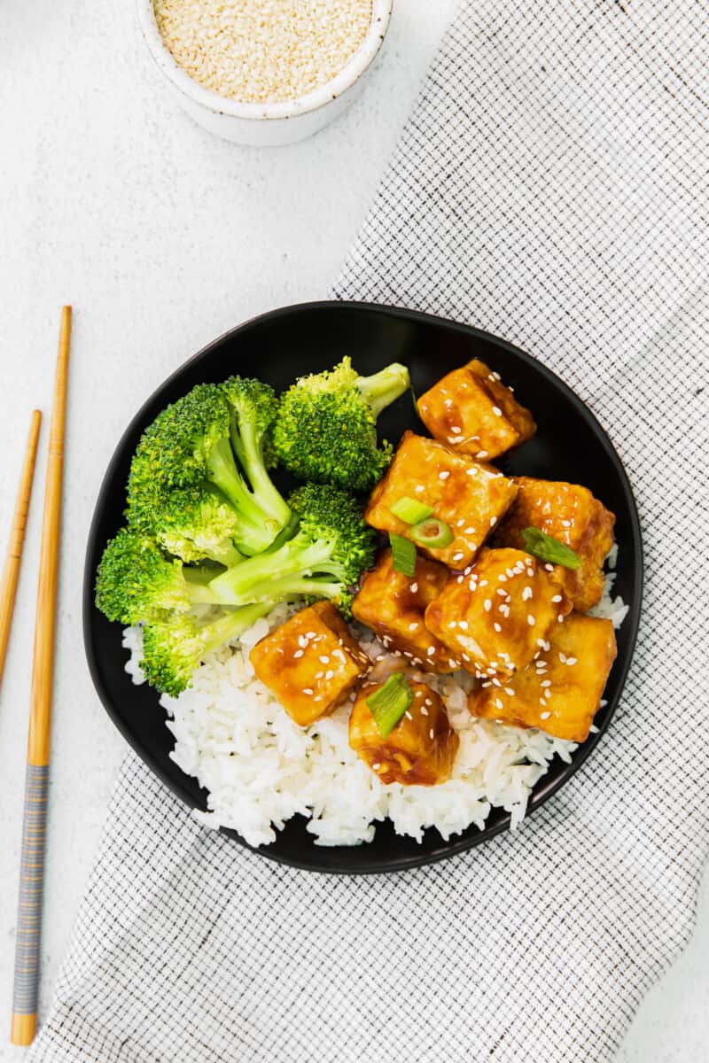 overhead view of air fryer teriyaki tofu on a black plate with chopsticks.