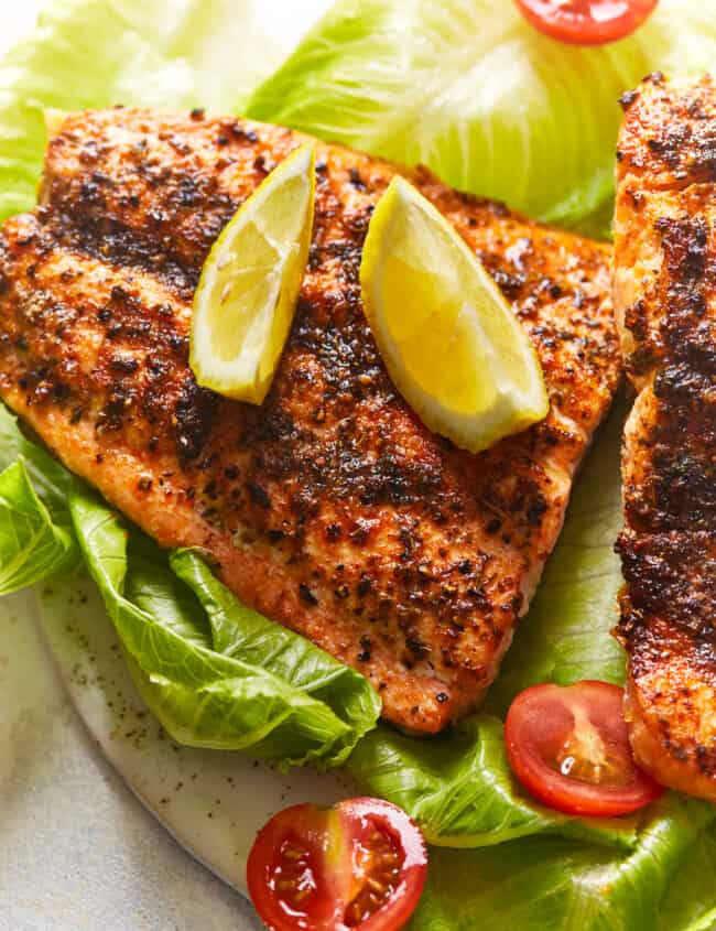 overhead view of an air fryer salmon filet on a bed of lettuce topped with lime wedges.