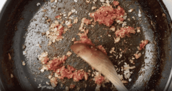 shallots in tomato paste in a skillet with a wooden spoon.