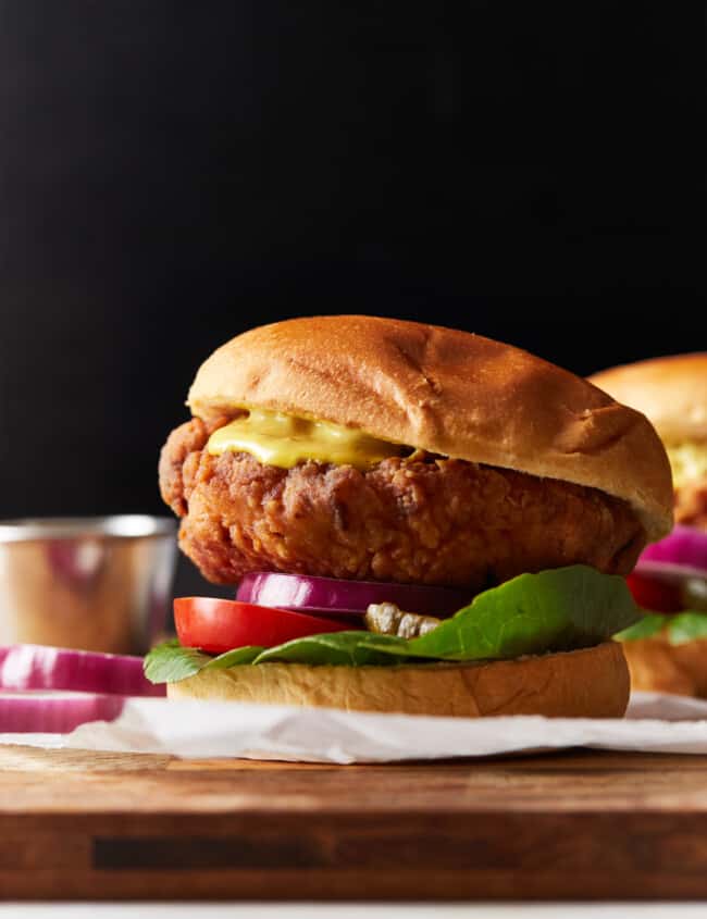 side view of a crispy chicken sandwich on a wooden cutting board.