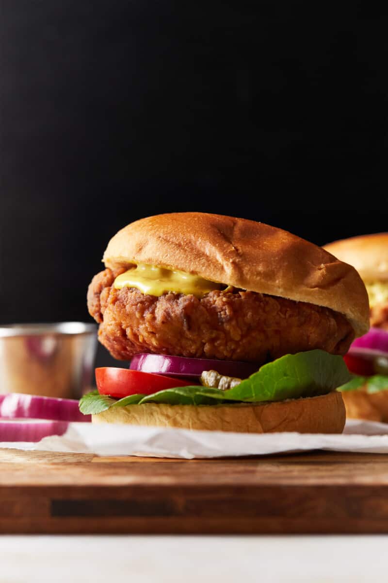 side view of a crispy chicken sandwich on a wooden cutting board.