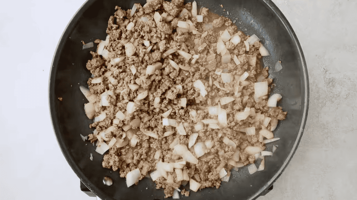 A frying pan filled with ground beef, onions, and Doritos for a casserole.