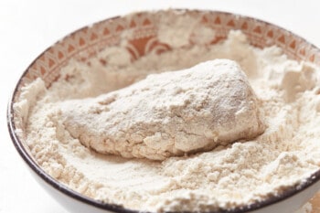 a piece of chicken dipped in seasoned flour in a white and red bowl.