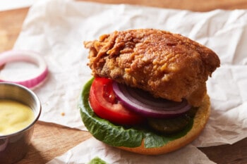 a partially assembled crispy chicken sandwich on a wooden cutting board.