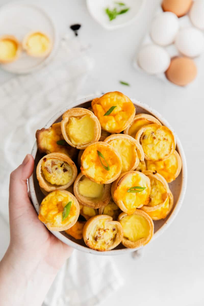 hand holding mini quiches on a white plate.