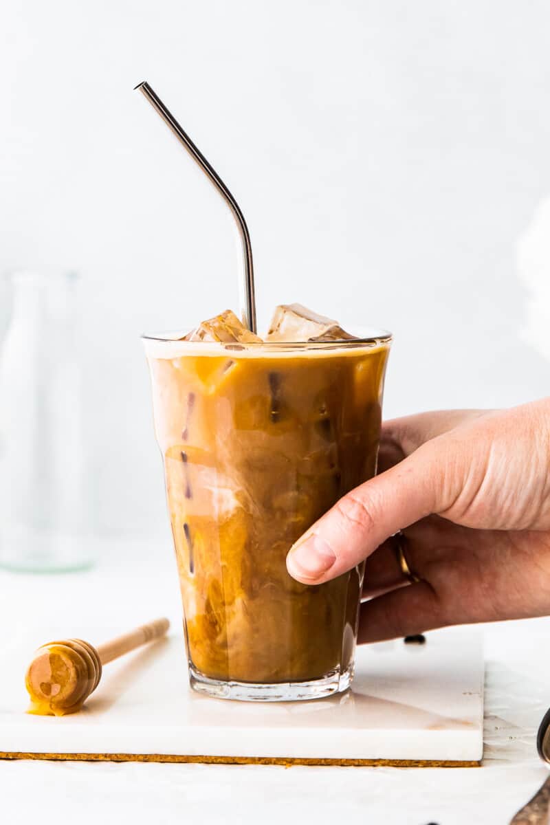 hand holding honey almondmilk flat white in clear glass with straw