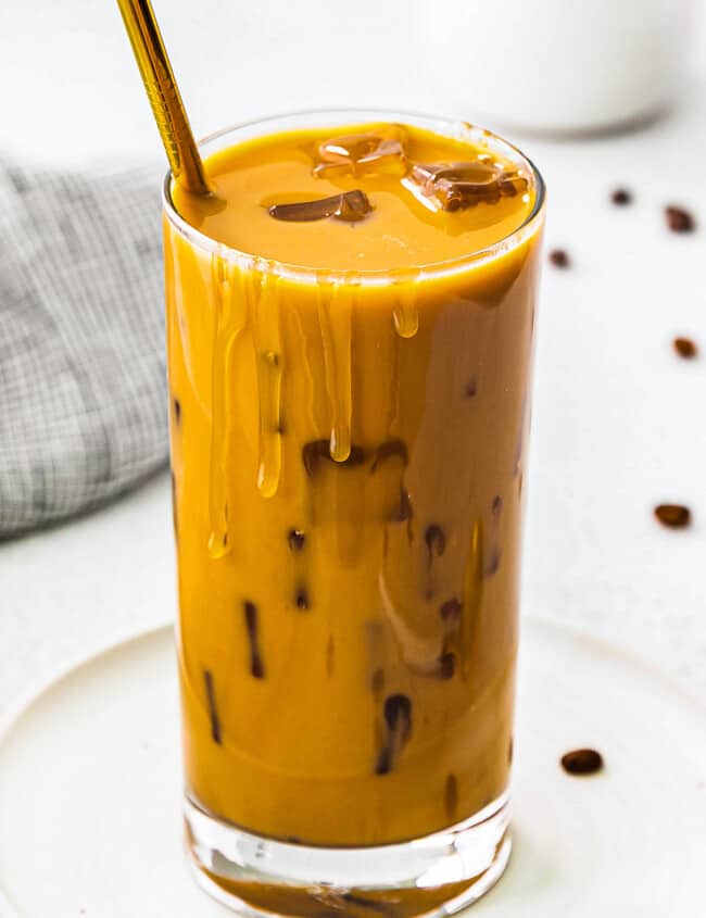 up close stirred iced caramel latte in glass with gold straw