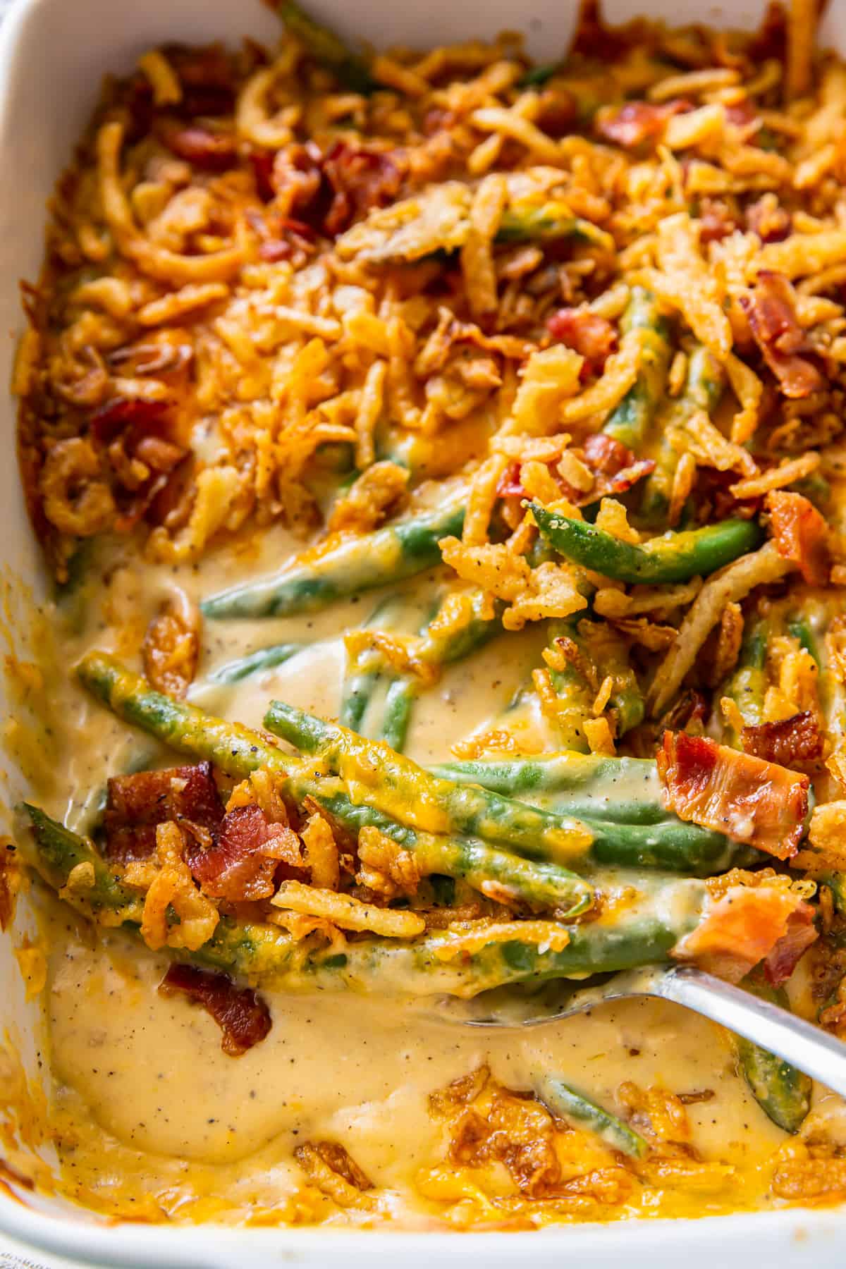 close up of cheesy green beans topped with fried onions and bacon.