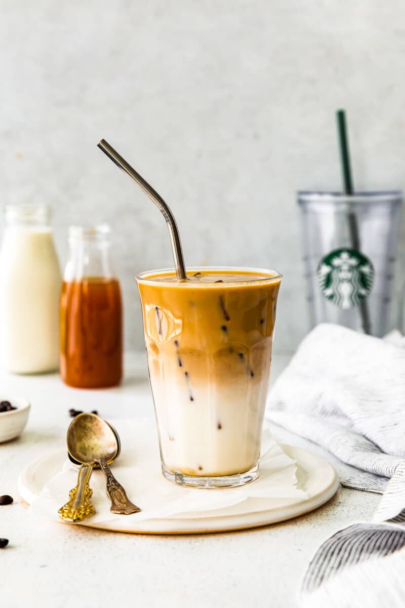 apple crisp macchiato in a clear glass on a white plate with a spoon and a straw