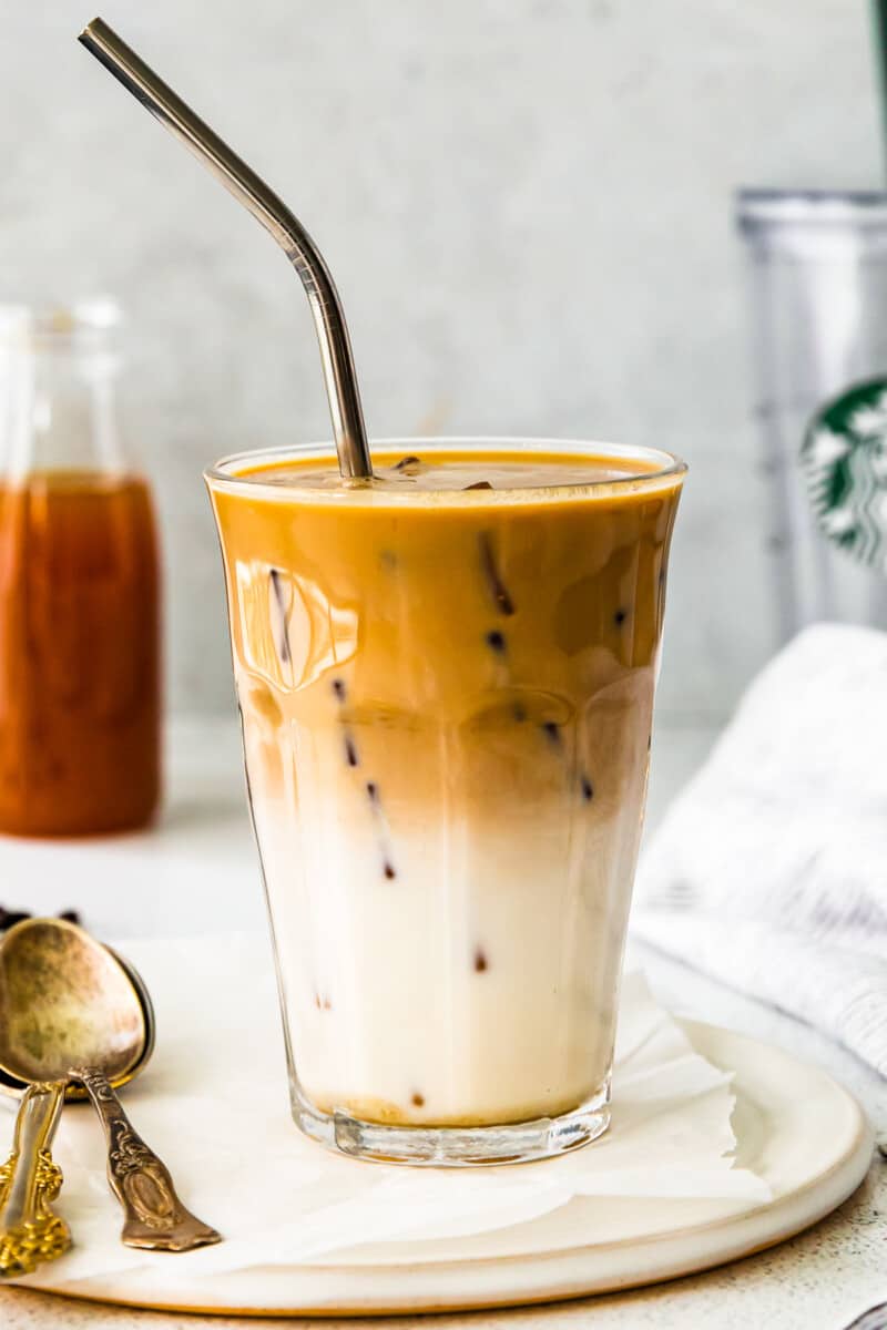 apple crisp macchiato in a clear glass on a white plate with a spoon and a straw