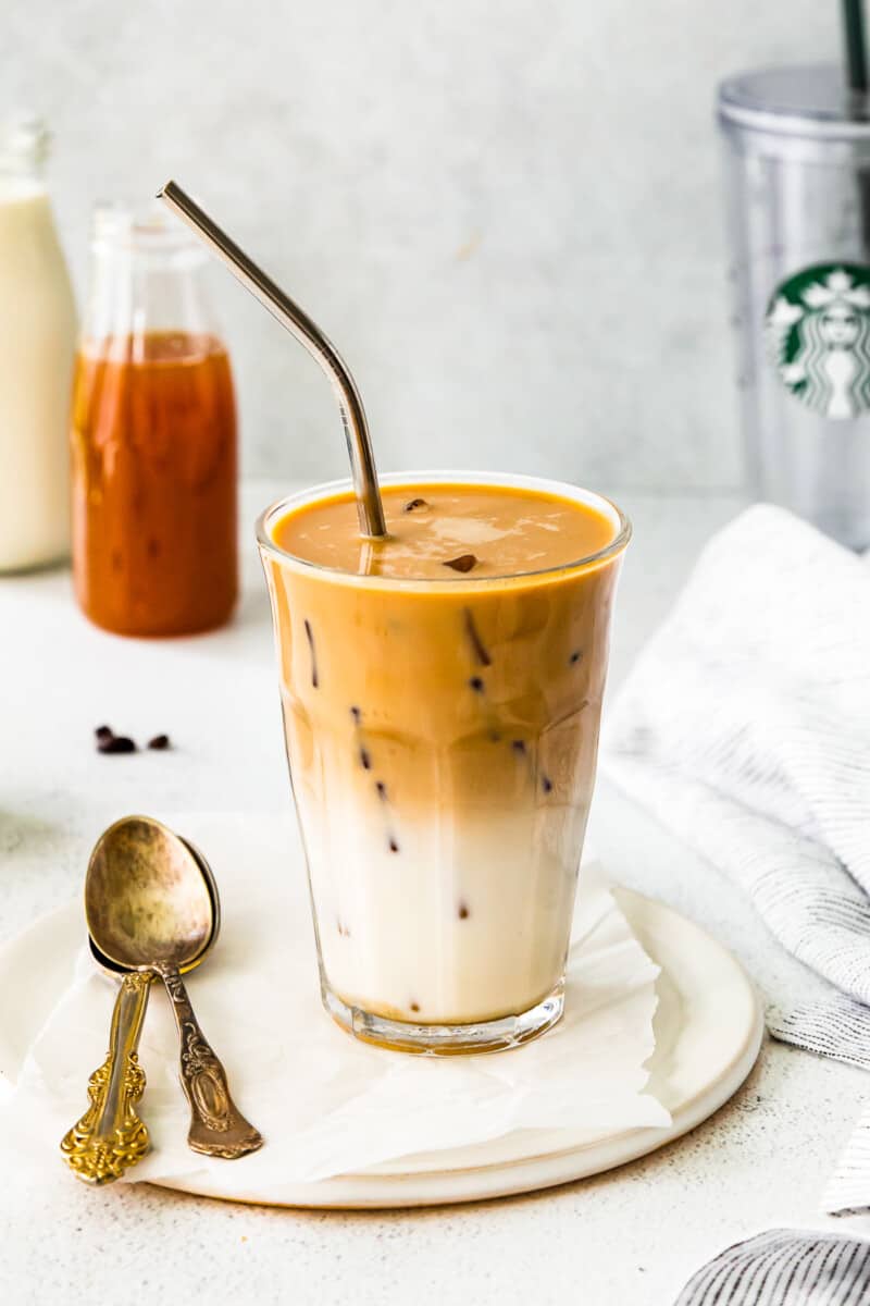 apple crisp macchiato in a clear glass on a white plate with a spoon and a straw