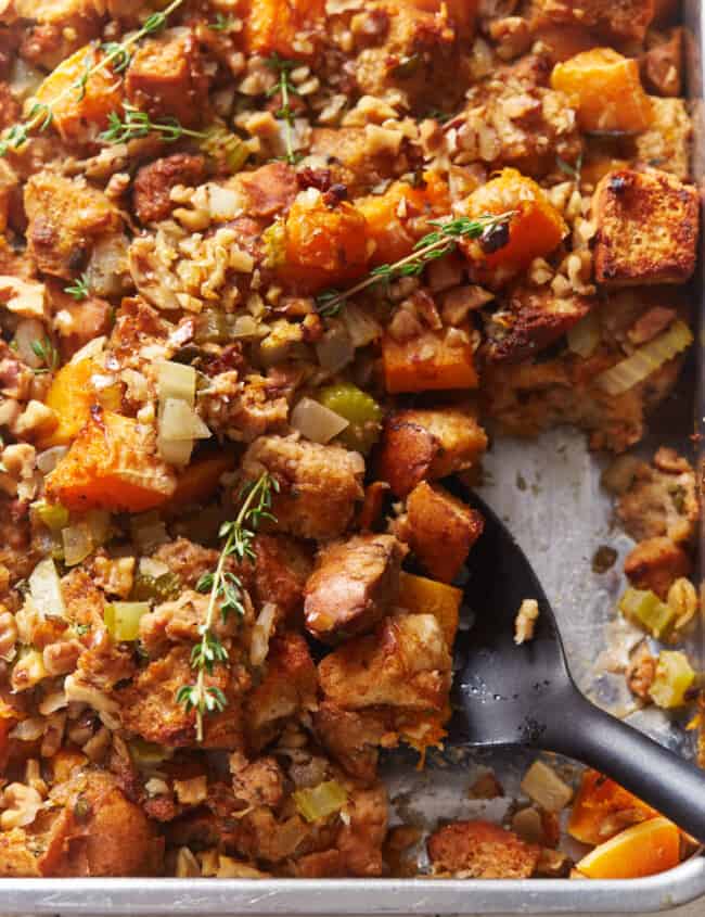 partial view of butternut squash stuffing in a baking pan with a black serving spoon.