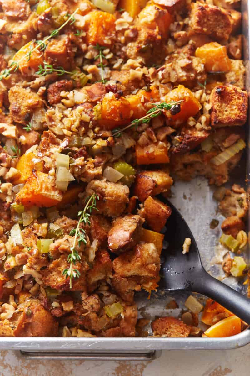 partial view of butternut squash stuffing in a baking pan with a black serving spoon.