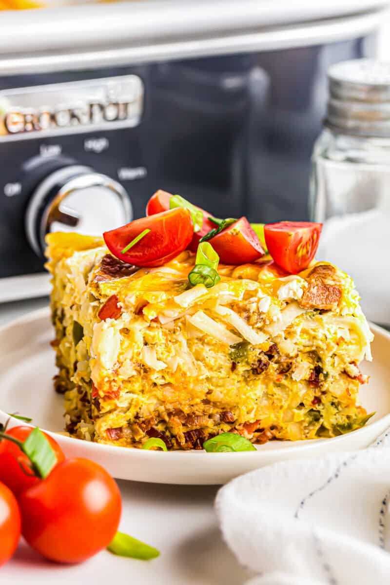 close up image of slice of breakfast casserole topped with diced tomatoes on a white plate