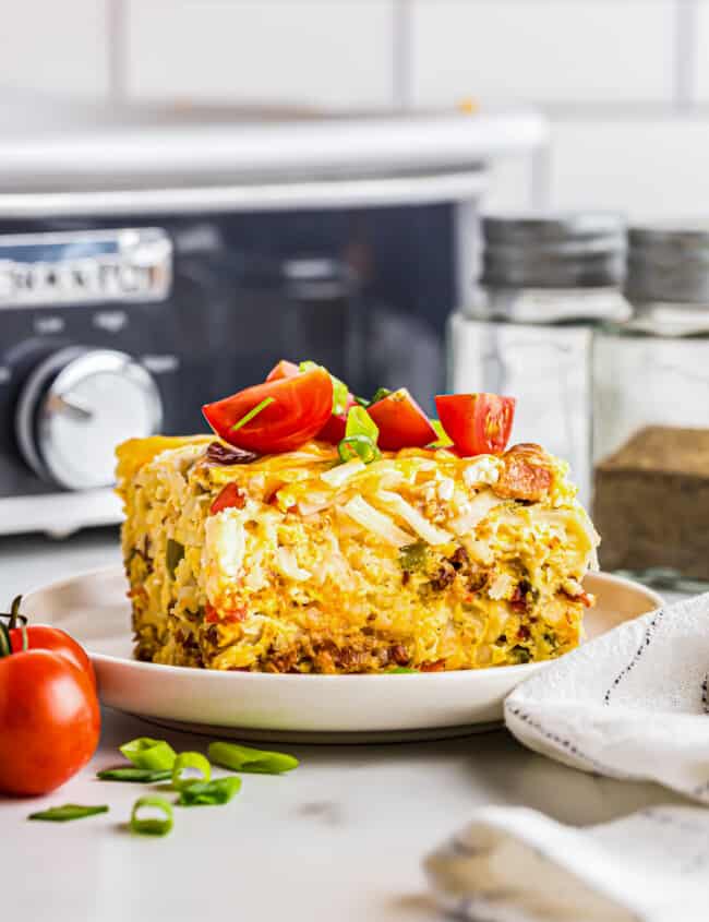 slice of breakfast casserole topped with diced tomatoes on a white plate