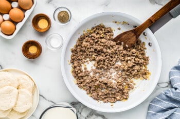 cooked crumbled sausage in a white skillet with a wood spoon