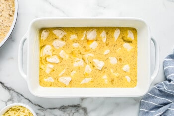 egg mixture on top of biscuit dough pieces in white baking dish