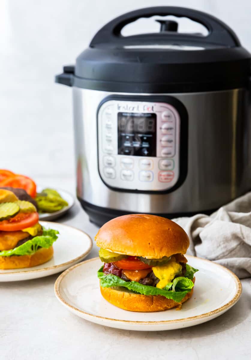 cheeseburgers on white plates in front of an instant pot