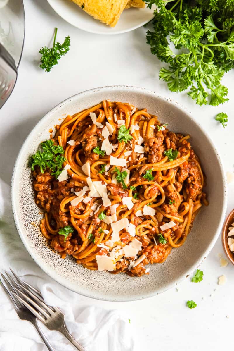 spaghetti topped with herbs and parmesan cheese in a white bowl