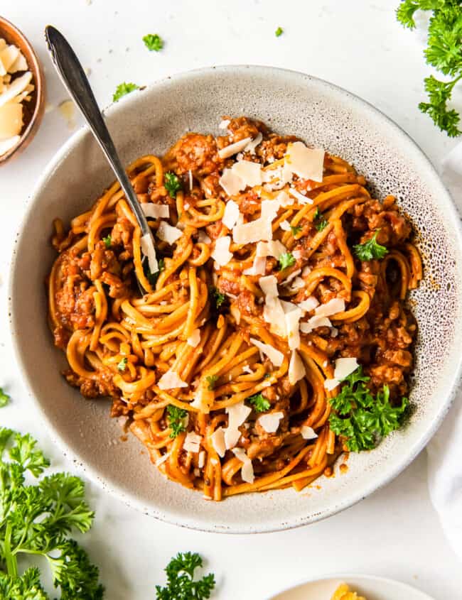 spaghetti topped with herbs and parmesan cheese in a white bowl with a fork