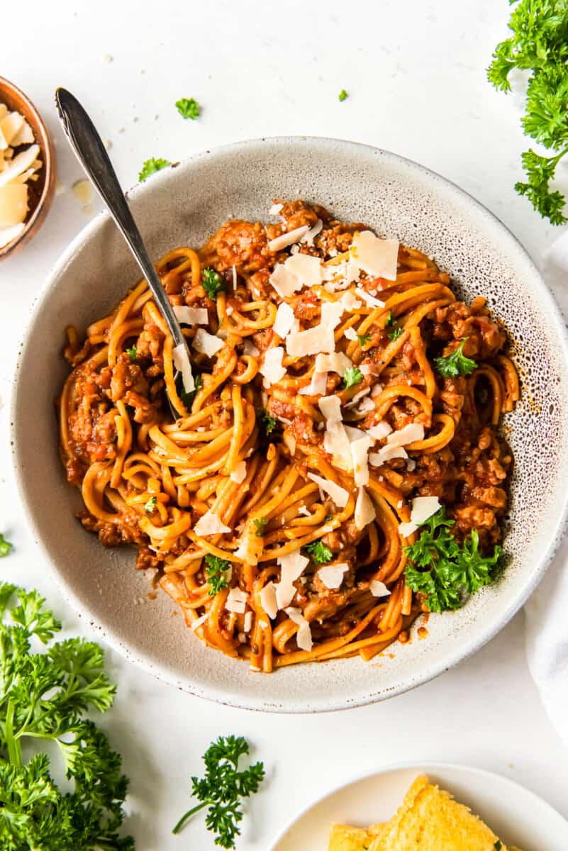 spaghetti topped with herbs and parmesan cheese in a white bowl with a fork