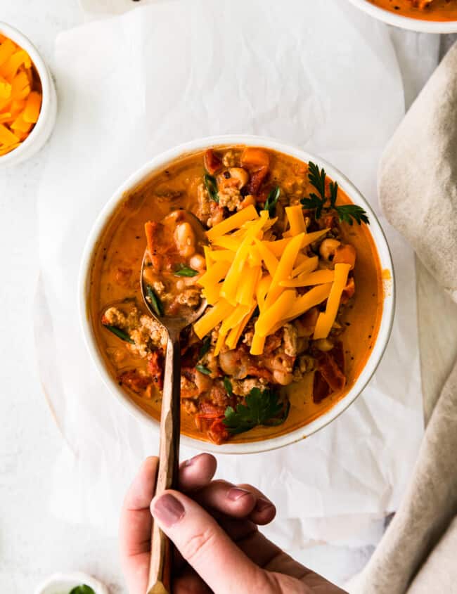 hand holding a spoon in a bowl of turkey white bean chili