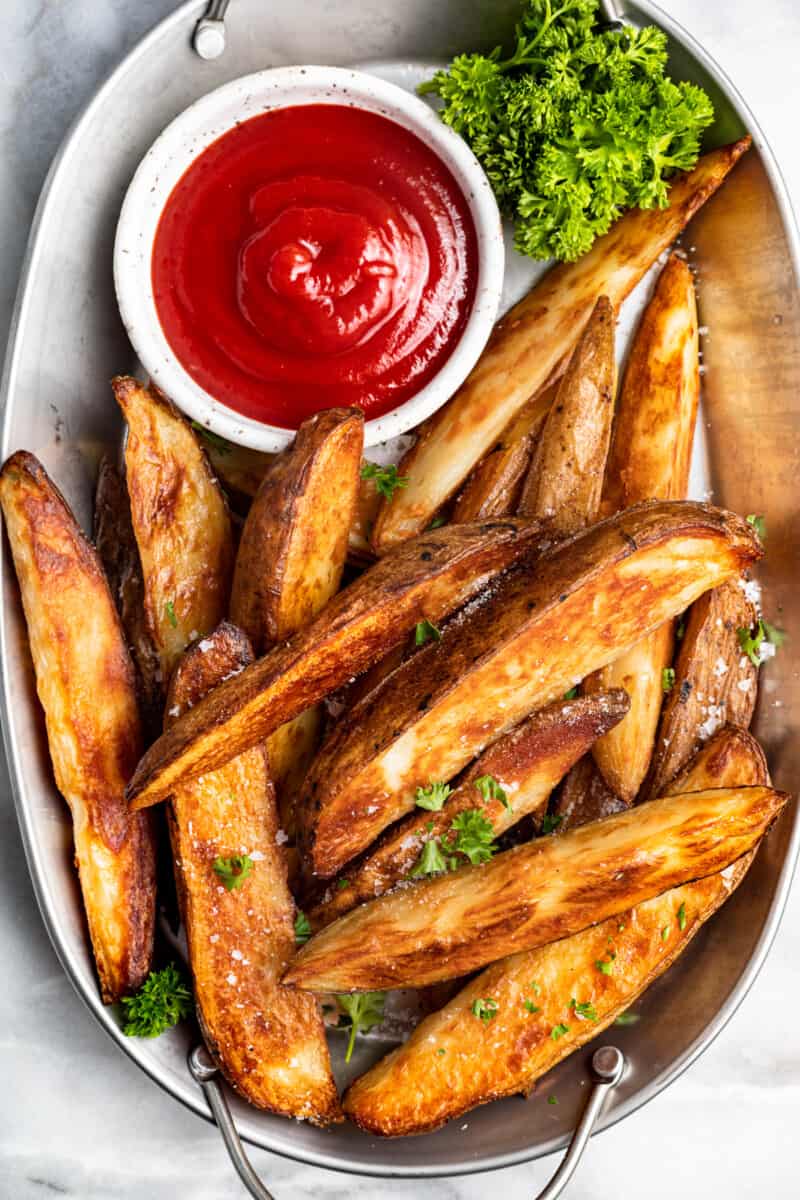 potato wedges on a white serving platter with ketchup in a white bowl