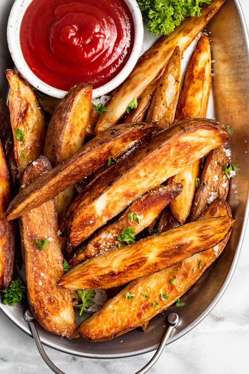 potato wedges on a white serving platter with ketchup in a white bowl