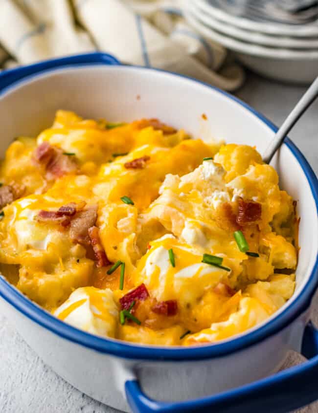 close up of loaded cauliflower bake in a blue and white casserole dish with a spoon.